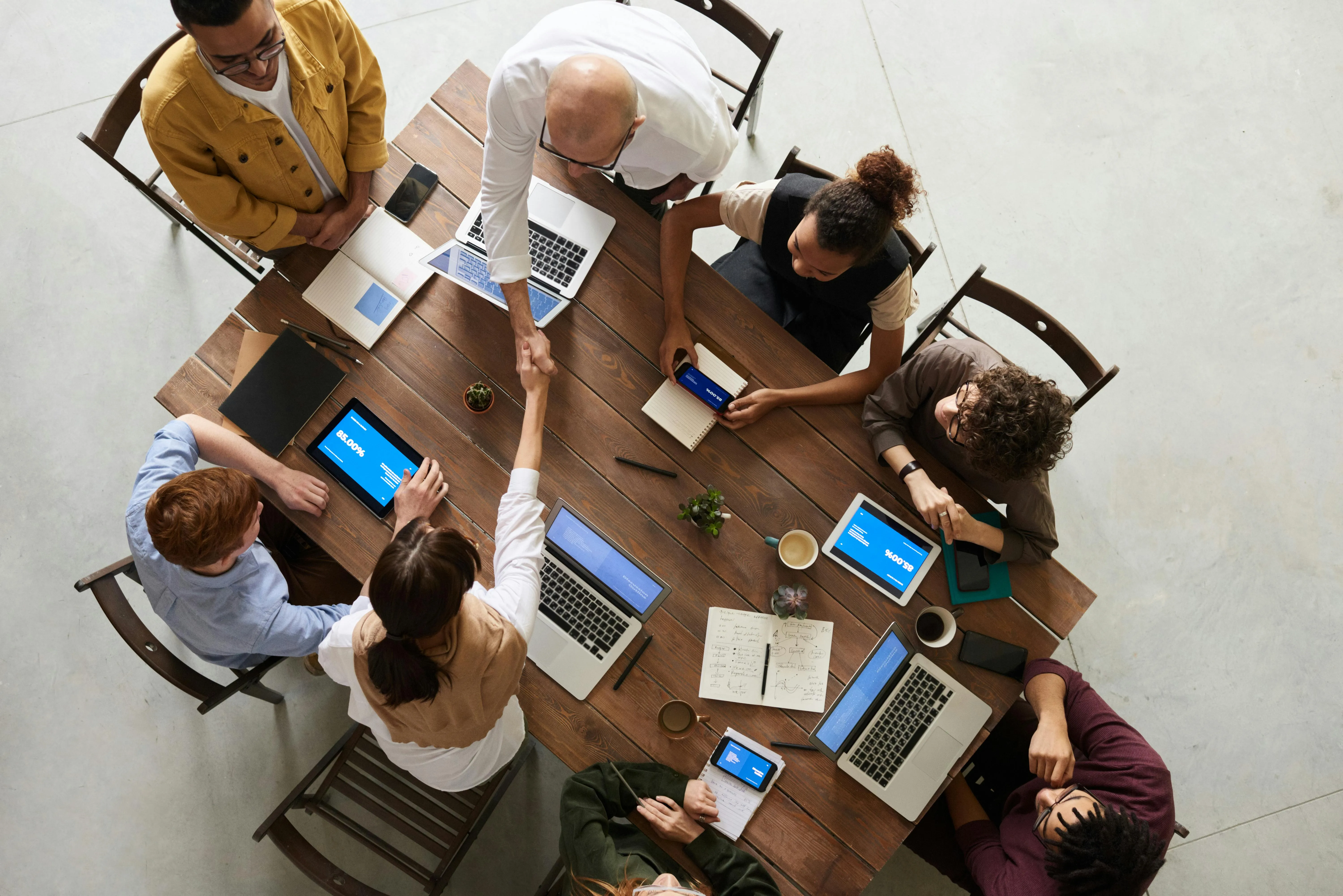 A confident professional woman leads a team meeting, gesturing toward a monitor while colleagues listen attentively, demonstrating leadership.