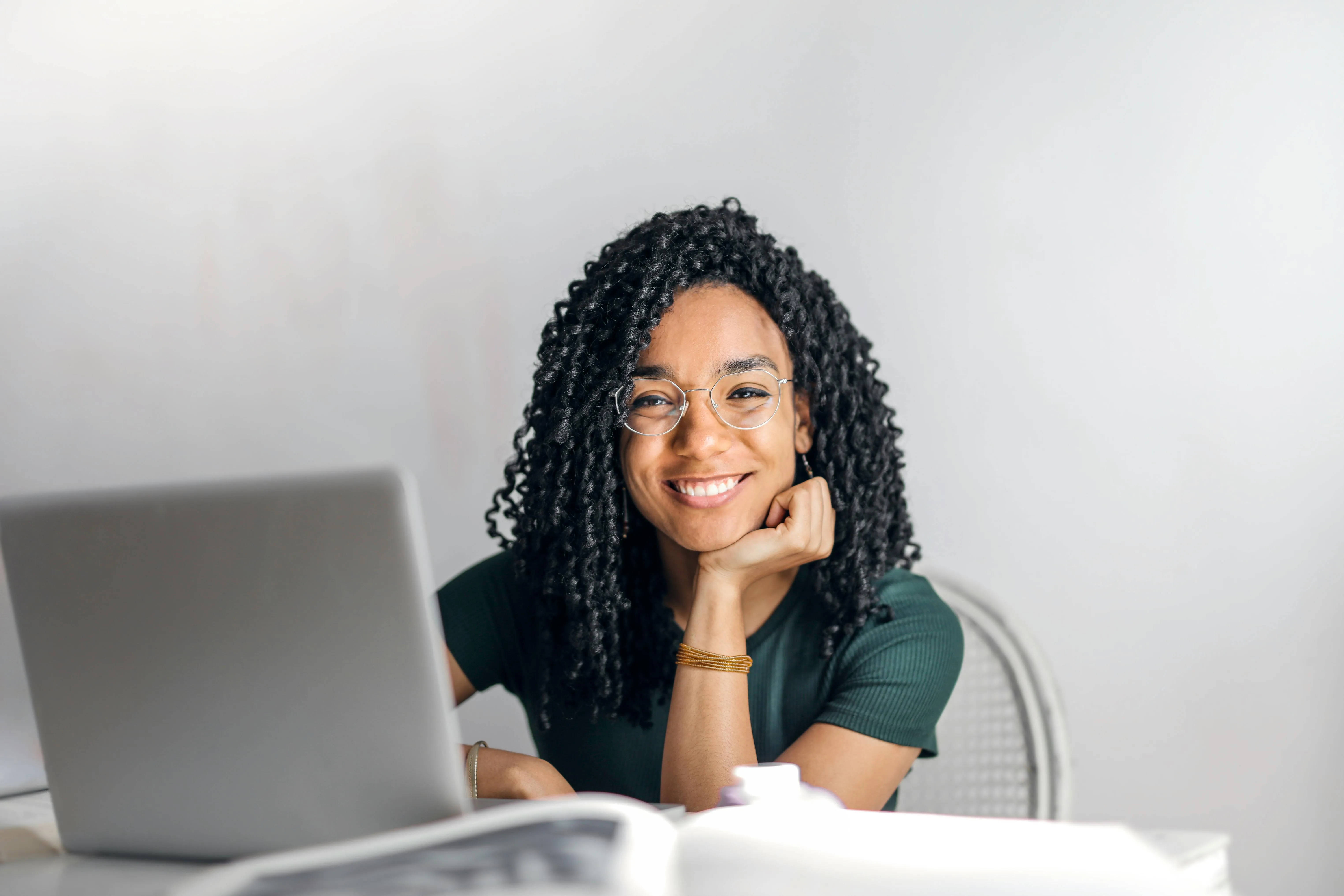 A confident, well-dressed young professional with glasses smiles while standing in a modern office environment.